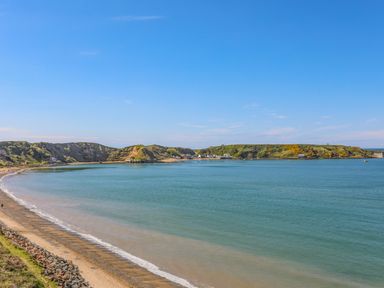 A view of a curved sandy beach with calm water and green hills in the background at Fairview Lodge in Pwllheli