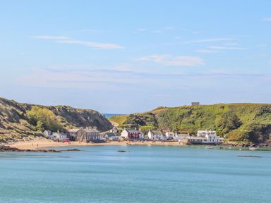 A small coastal village with buildings along a sandy beach and green hills in the background at Fairview Lodge in Pwllheli