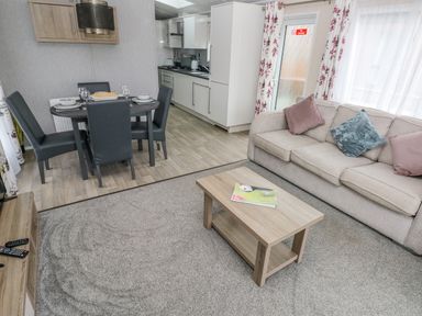 A living room with a beige sofa and coffee table next to a dining area with a round table and four chairs at Starfish Retreat in Little Haven near Broad Haven