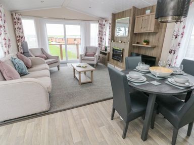 A living room with a sofa, armchairs, coffee table, dining table with chairs and tableware at Starfish Retreat in Little Haven near Broad Haven
