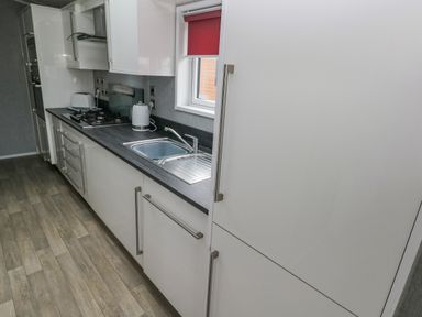 A kitchen with white cabinets a black countertop a sink a cooker a toaster and a window with a red blind at Starfish Retreat in Little Haven near Broad Haven