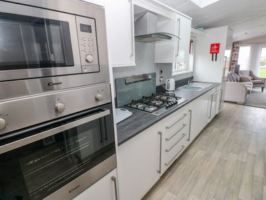 A kitchen with built in microwave and oven gas hob kettle sink and white cabinets with living room in the background at Starfish Retreat in Little Haven near Broad Haven
