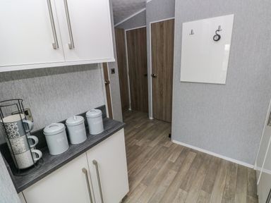 A kitchen corner with white cabinets wooden floor and three doors in the hallway at Starfish Retreat in Little Haven near Broad Haven