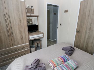 A bedroom with a bed with folded towels a wardrobe a small TV and a wooden door at Starfish Retreat in Little Haven near Broad Haven