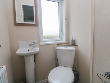 A bathroom with a pedestal sink a toilet a small mirror and a window at Starfish Retreat in Little Haven near Broad Haven