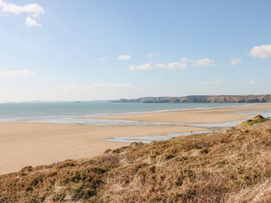 A wide sandy beach with calm sea and hills in the distance at Starfish Retreat in Little Haven near Broad Haven