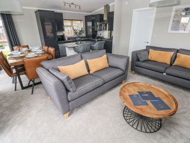 A living room with two grey sofas, a wooden coffee table, and a dining table with brown chairs next to a kitchen at Driftwood Lodge in Hasguard Cross near Broad Haven