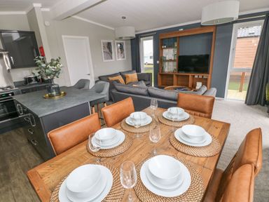 A dining table set with plates bowls and glasses next to a kitchen island and living room at Driftwood Lodge Hasguard Cross near Broad Haven