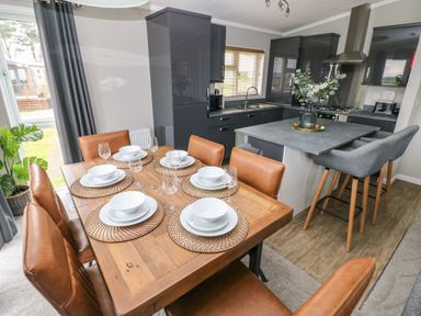 A dining area with leather chairs and place settings next to a kitchen with gray cabinets and a breakfast bar at Driftwood Lodge in Hasguard Cross near Broad Haven