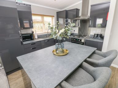 A kitchen with grey cabinets a countertop island with a vase of flowers two chairs microwave toaster and gas stove at Driftwood Lodge Hasguard Cross near Broad Haven