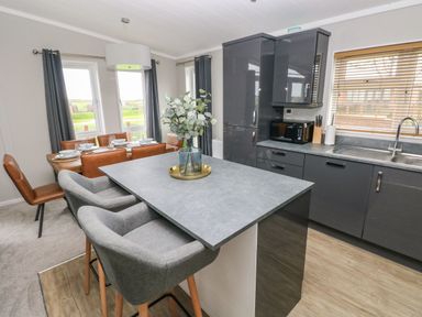 A kitchen and dining area with gray cabinets a dining table with brown chairs and a kitchen island with gray stools at Driftwood Lodge in Hasguard Cross near Broad Haven