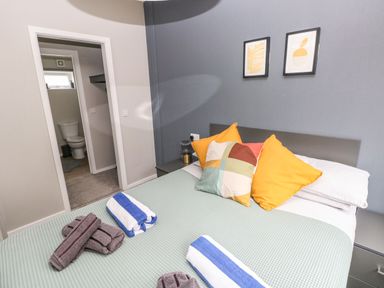 A bedroom with a bed with pillows and folded towels and a bathroom visible through an open door at Driftwood Lodge in Hasguard Cross near Broad Haven