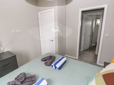 A bedroom with a bed covered with a green bedspread and rolled towels near a door leading to a bathroom at Driftwood Lodge Hasguard Cross near Broad Haven