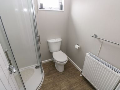 A bathroom with a shower cubicle a toilet a radiator and a window at Driftwood Lodge in Hasguard Cross near Broad Haven