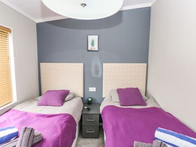 A bedroom with two single beds with purple blankets and pillows and a small nightstand between them at Driftwood Lodge in Hasguard Cross near Broad Haven