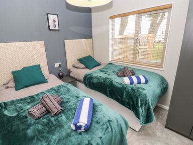 A bedroom with two single beds green blankets and rolled towels on beds at Driftwood Lodge in Hasguard Cross near Broad Haven