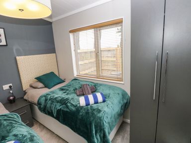 A bedroom with two single beds green blankets and a window with blinds at Driftwood Lodge Hasguard Cross near Broad Haven