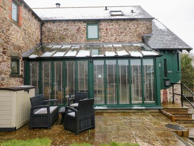 A stone house with a glass conservatory and outdoor seating at Skomer Cottage Sandy Haven near Milford Haven