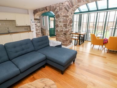 A living room with a blue sectional sofa exposed stone arches and a dining area with yellow chairs at Skomer Cottage in Sandy Haven near Milford Haven