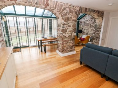 A room with stone arches wooden dining table with benches yellow chairs and a gray sofa at Skomer Cottage in Sandy Haven near Milford Haven