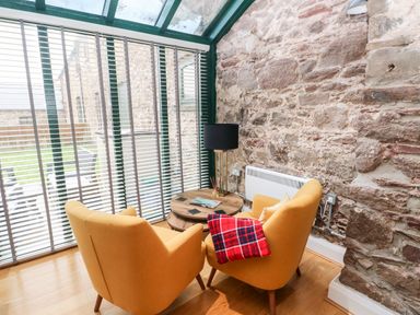 A sunroom with two yellow armchairs around a wooden coffee table against a stone wall at Skomer Cottage Sandy Haven near Milford Haven