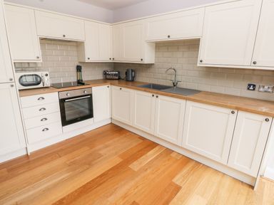 A kitchen with white cabinets wooden countertops an oven a microwave a toaster a kettle and a sink at Skomer Cottage in Sandy Haven near Milford Haven