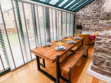 A dining area with a wooden table set for six and a bench next to a stone wall at Skomer Cottage in Sandy Haven near Milford Haven