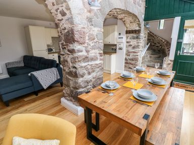 A dining area with a set table a stone archway and a living area with a blue sofa at Skomer Cottage Sandy Haven near Milford Haven