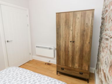 A bedroom corner with a wooden wardrobe a white door a wall-mounted heater and a patterned bedspread at Skomer Cottage in Sandy Haven near Milford Haven