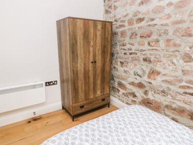 A wooden wardrobe next to a stone wall and a bed with patterned bedding in a bedroom at Skomer Cottage in Sandy Haven near Milford Haven
