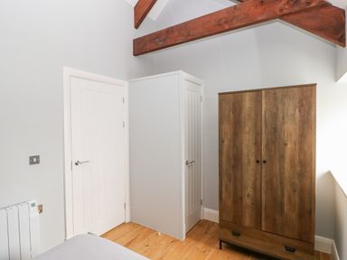 A bedroom corner with a wooden wardrobe a white radiator and two white doors under a wooden beam ceiling at Skomer Cottage in Sandy Haven near Milford Haven