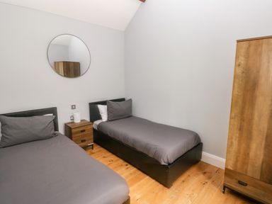 A bedroom with two single beds a wooden nightstand with a lamp a round mirror and a wooden wardrobe at Skomer Cottage in Sandy Haven near Milford Haven