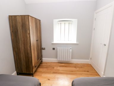 A bedroom with a wooden wardrobe a small window with blinds a white radiator a closed white door and parts of two beds at Skomer Cottage in Sandy Haven near Milford Haven