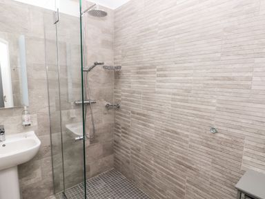 A bathroom with a glass shower partition a rain shower head a sink with a soap dispenser and tiled walls and floor at Skomer Cottage in Sandy Haven near Milford Haven