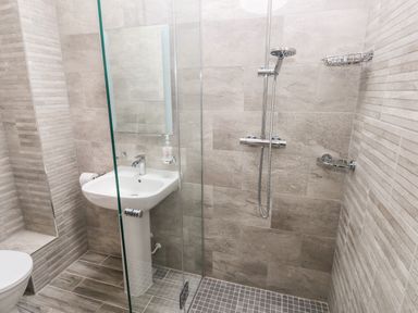 A bathroom with a shower area separated by glass a pedestal sink a wall-mounted mirror and a toilet at Skomer Cottage Sandy Haven near Milford Haven