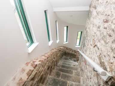A stone staircase with narrow vertical windows along the curved wall at Skomer Cottage in Sandy Haven near Milford Haven