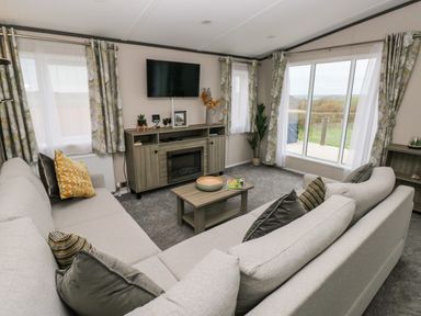 A living room with beige sofas a wooden coffee table a wall-mounted television and large windows at Ramsey in Broad Haven