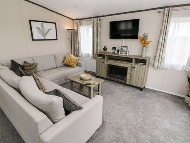 A living room with two sofas a coffee table a TV on the wall and a cabinet with a fireplace at Ramsey in Broad Haven
