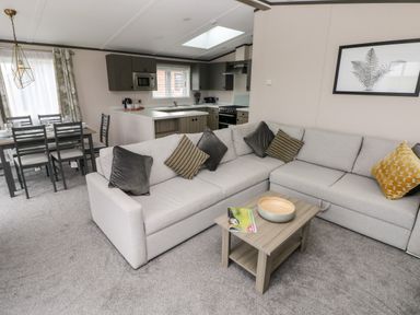 A living room with a gray sectional sofa and coffee table connected to a kitchen and dining area at Ramsey in Broad Haven
