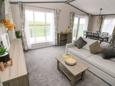 A living room with a sofa coffee table and dining area with large windows and curtains at Ramsey in Broad Haven