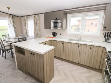 A kitchen with wooden cabinets white countertop an integrated microwave and a dining table with chairs at Ramsey in Broad Haven