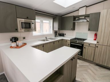 A kitchen with white countertops wooden cabinets a microwave oven stove sink toaster and a fire extinguisher at Ramsey in Broad Haven