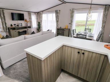 An open-plan living area with a sofa, a wall-mounted TV, a dining table set for six, and a kitchen counter at Ramsey in Broad Haven