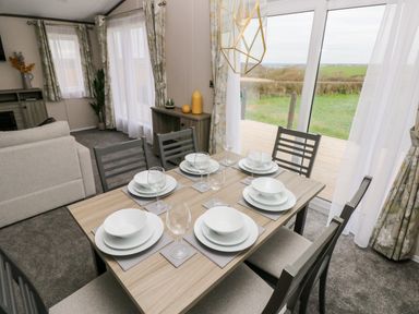 A dining table set with plates and glasses next to a sliding glass door with curtains at Ramsey in Broad Haven
