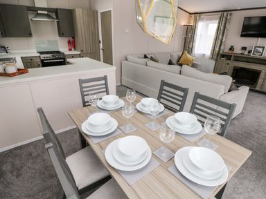 A dining table set with white plates and glasses next to a kitchen and a living room with a sofa and television at Ramsey in Broad Haven