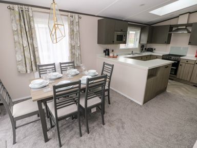 A dining area with a table set for six and a kitchen with cabinets and appliances at Ramsey in Broad Haven