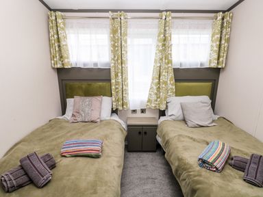 A bedroom with two single beds with pillows and folded towels and a bedside table under curtained windows at Ramsey in Broad Haven