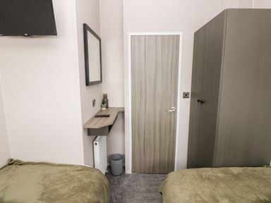 A bedroom with two beds covered with green blankets a wooden door a wall mounted TV and a wooden wardrobe at Ramsey in Broad Haven