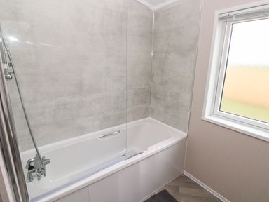 A bathroom with a bathtub shower and a frosted window at Ramsey in Broad Haven