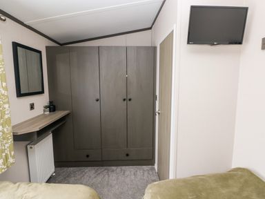 A bedroom with a wardrobe a wall-mounted tv a wooden door a small desk and a wall mirror at Ramsey in Broad Haven